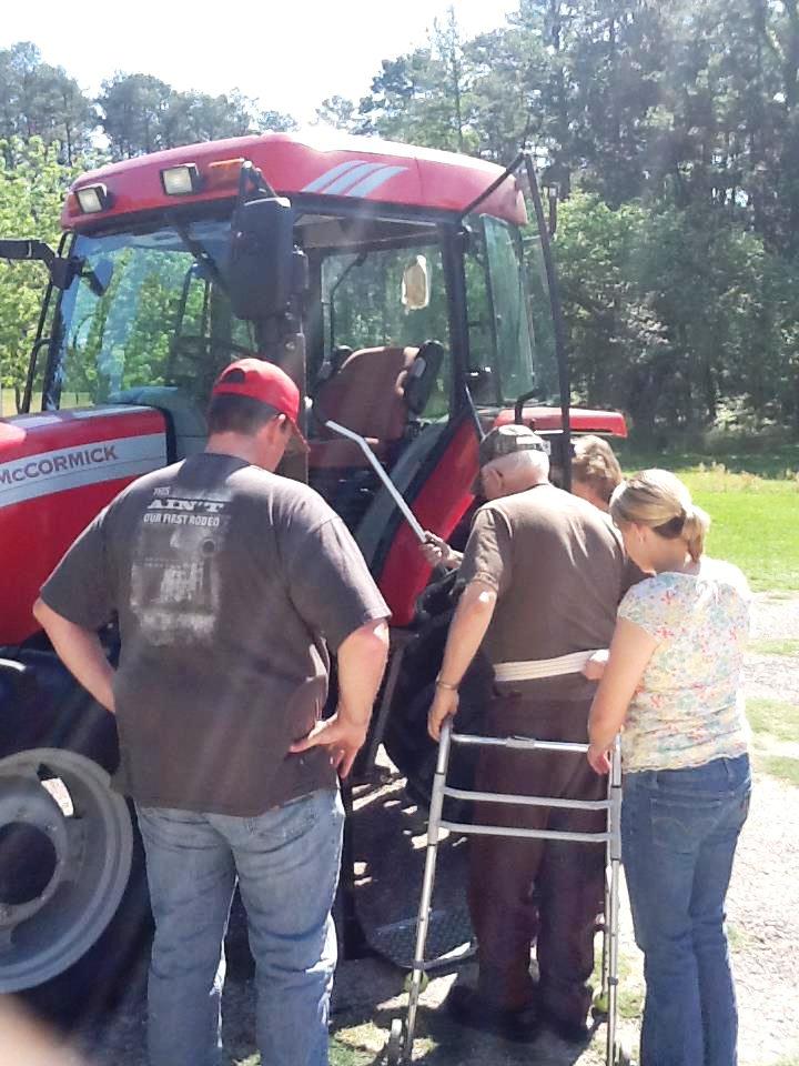 Disabled farmer getting onto tractor with the aid of  two other people. 