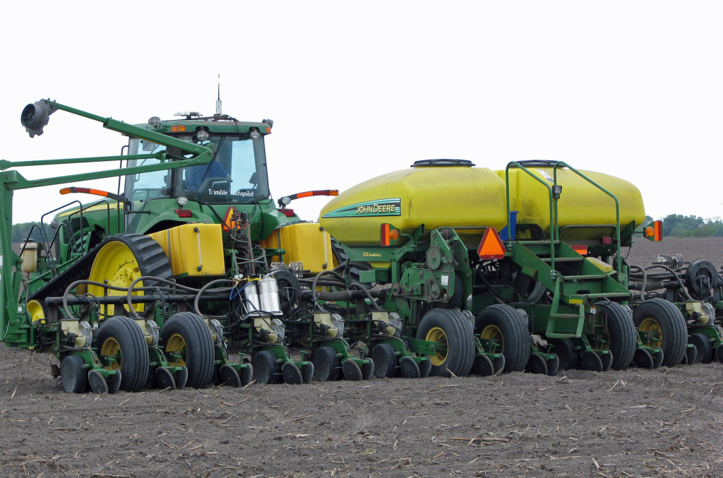 A green tractor with yellow tanks and other farm equipment in field