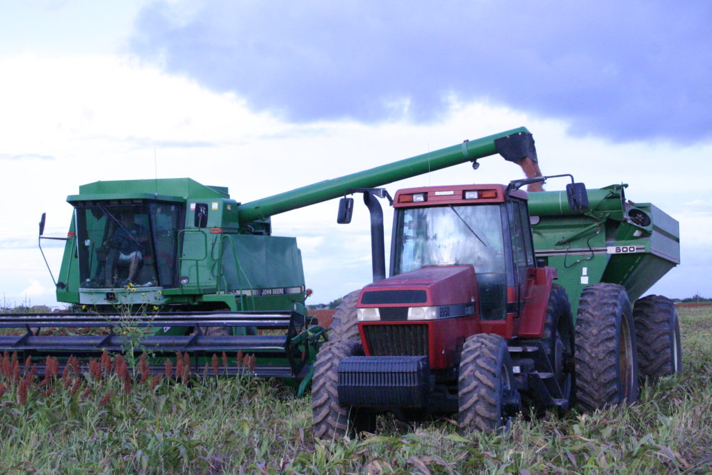 A green combine unloads grain into a red tractor pulling a grain cart