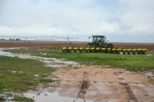 A tractor with a planter sits next to a wet field. 