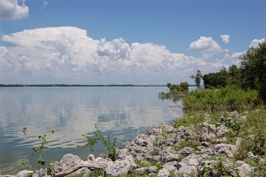 Lavon Lake in Texas. A blue sky with white clouds is reflected in the still waters of a large lake