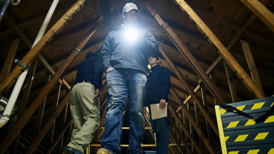 Exterminator searching attic with flashlight