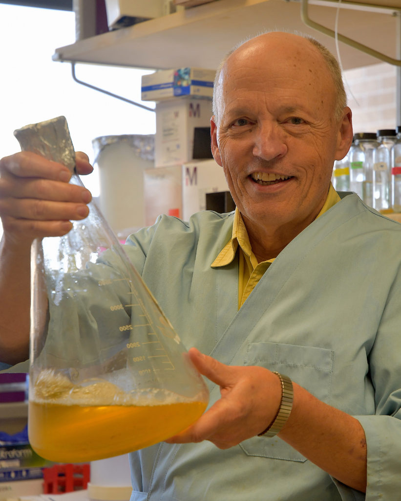 A man, Ryland Young, holding up a large beaker with a colored liquid in the bottom of it