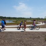 Children riding bikes along a paved path next to a pond