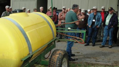Pesticide applicator spray rig, yellow tank or green trailer, being discussed during training.