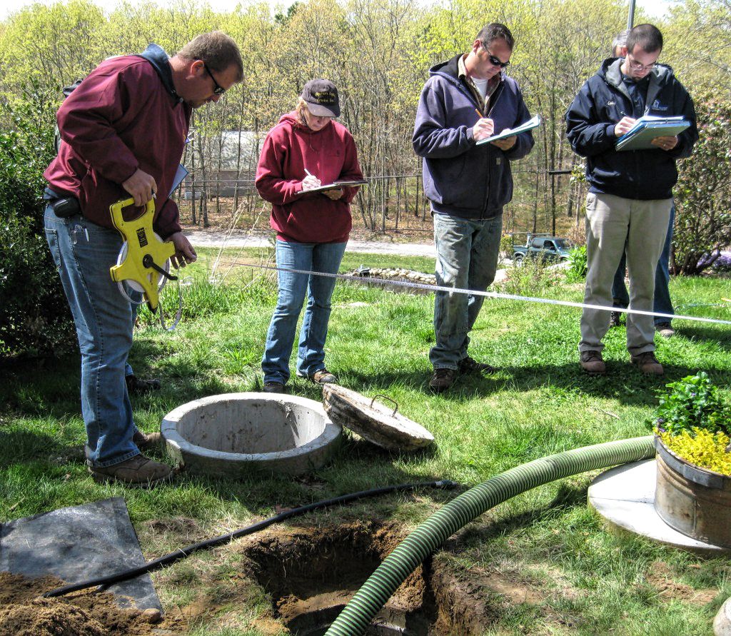 A group of people standing outside and an open septic hole, checking the septic system
