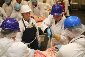 Four adults in hard hats processing a cut of beef