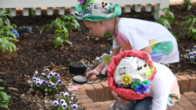 Two children search the garden using magnifying glasses and wearing their new sombreros.