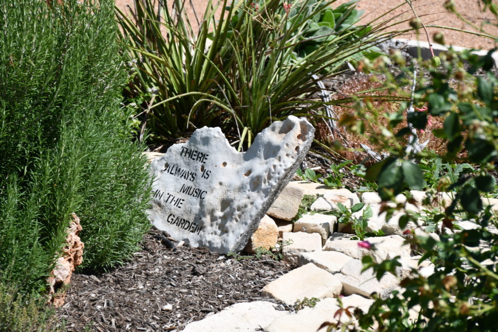 Rocks and plants in the Concho Valley Texas Master Gardeners Demonstration Garden.  A stone bears a writing that says there is always music in the garden.