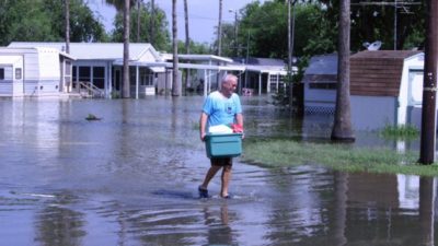 Edlerly man walks through water with his personal belongings
