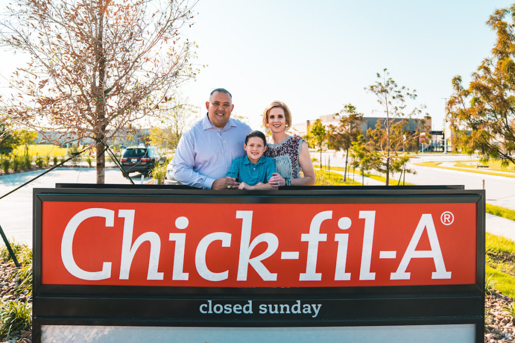 Headshot of Hayley and Jerald Huggins and son over Chick Fil A sign