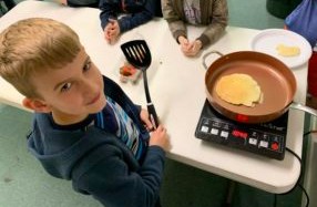 a young man cooks a pancake on portable cooktop during a 4-H family program