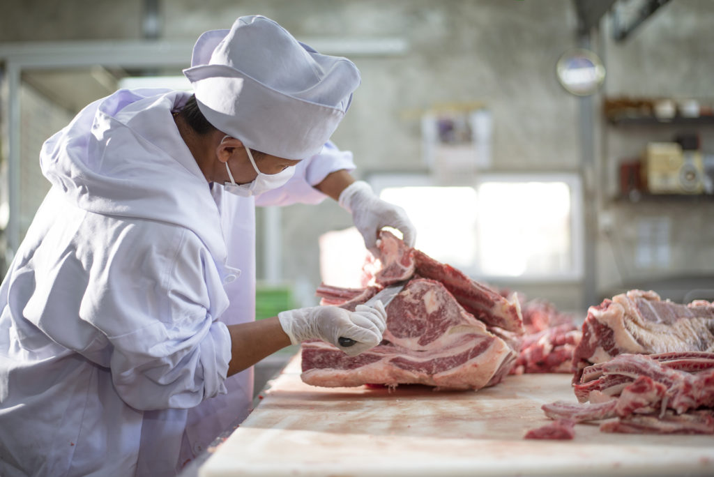 Masked man in white uniform cutting meat