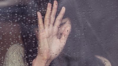 Girl with her hand in front of her face, behind a window with rain drops