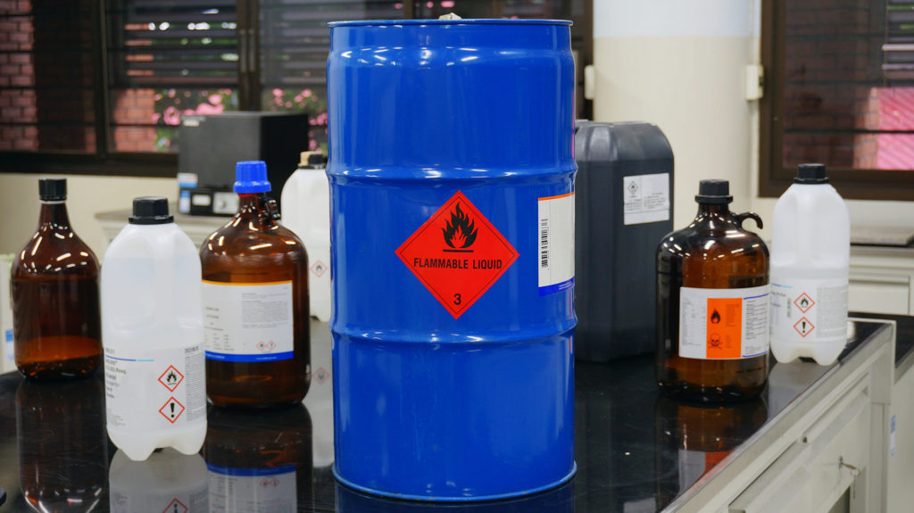 blue barrel with red caution diamond surrounded by other agricultural pesticide waste containers