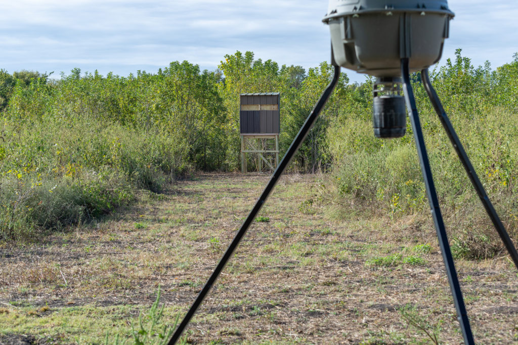 a deer feeder in the foreground with a hunting blind in the background