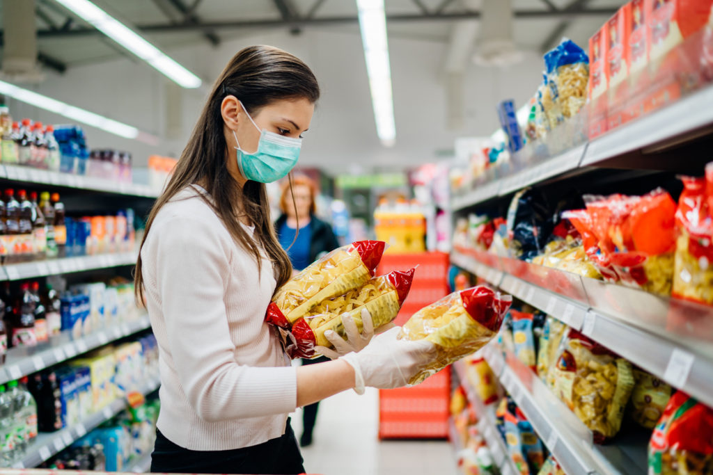 Woman buying few pasta packages during COVID-19 pandemic indicated by mask.