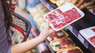 Close up of woman holding beef in grocery store.