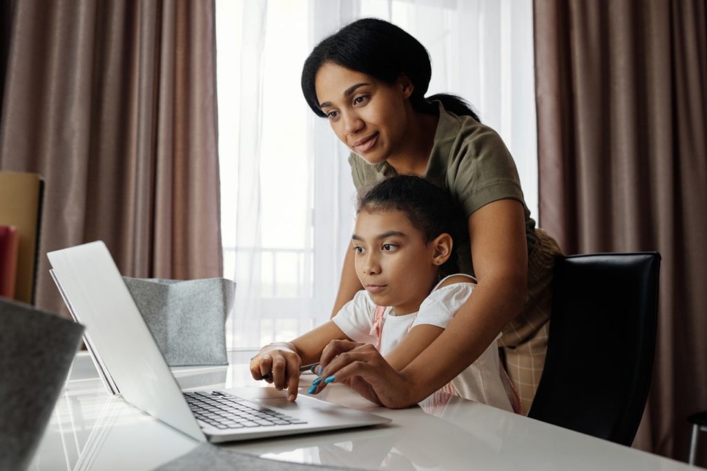 Woman helping a child at a laptop at a kitchen table - depicting child care conference subject matter