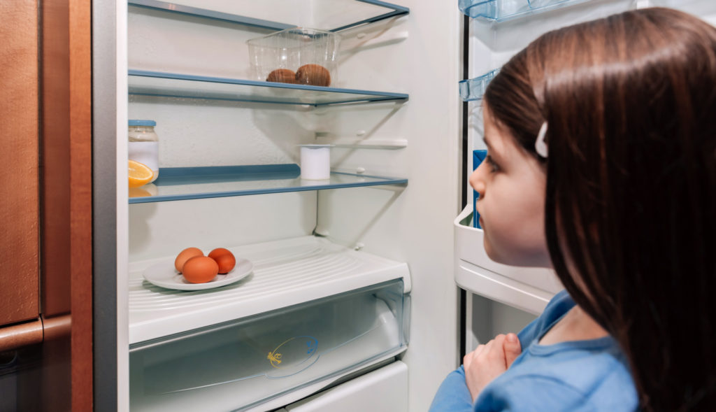 Worried girl looking at the almost empty fridge due to food insecurity