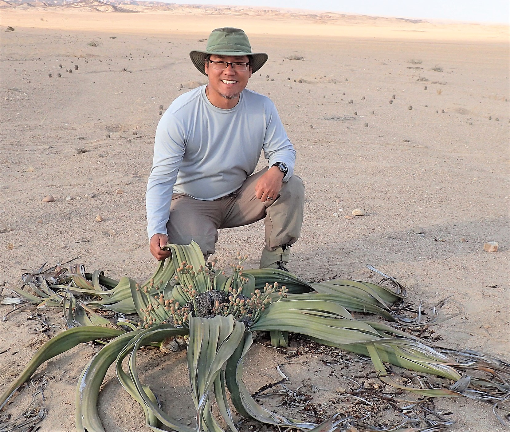A man with a hat on, Hojun Song, Ph.D., in front of a dried plant on a cricket collecting expedition.