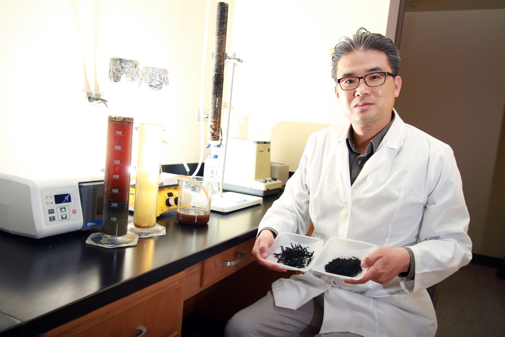 Eunsung Kan sits in a lab coat in his lab with two kinds of biochar