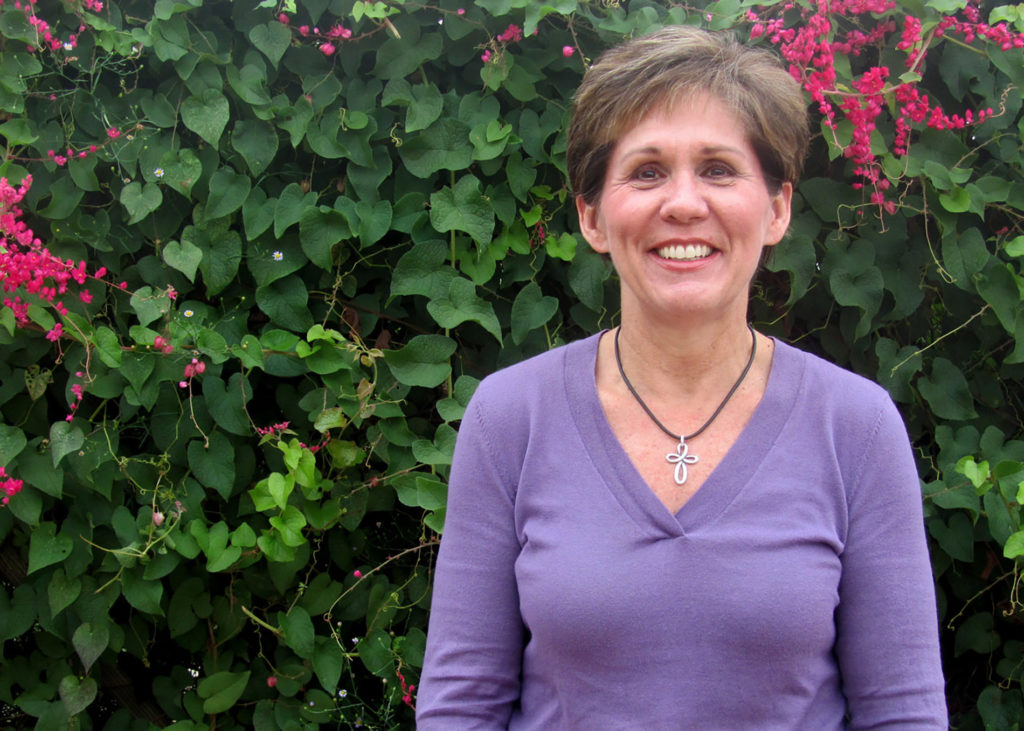 Woman, Patricia Klein, in purple shirt standing in front of greenery.