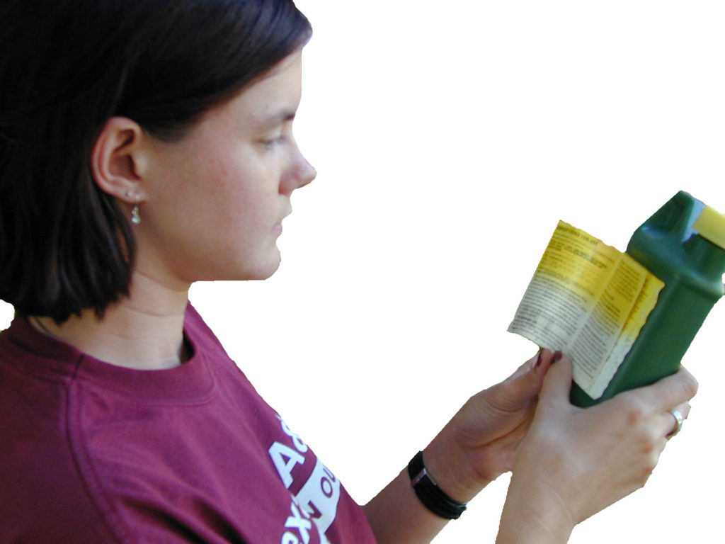 Woman in Aggie t-shirt reading a pesticide bottle label