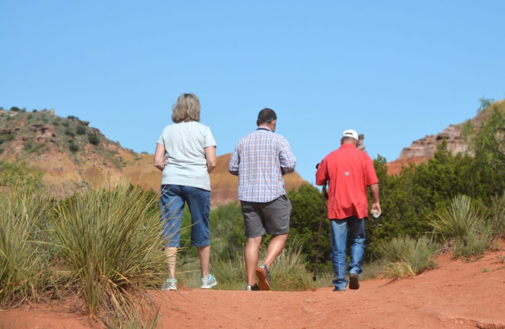Three hikers traveling down a red dirt path