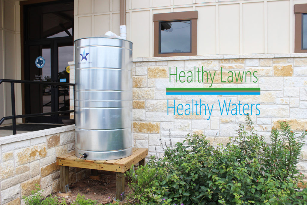 Photo of the front of a building with a cistern near the door and the "Healthy Lawns, Healthy Waters" logo on the wall. The program teaches rainwater harvesting and turf management in Texas