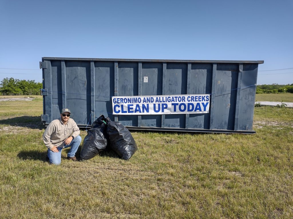 Participant in front of a dumpster with a sign on it reading Geronimo and Alligator Creeks Clean Up Today