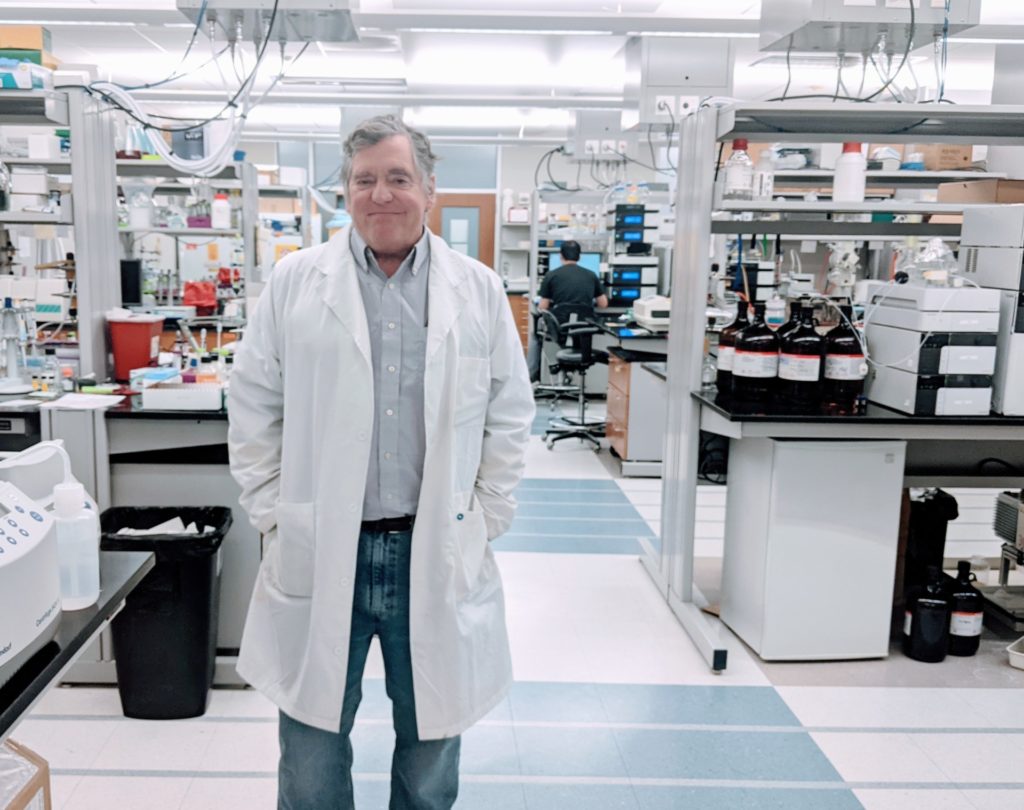 A man in a white lab coat, Dr. Thomas Meek, stands in a laboratory setting