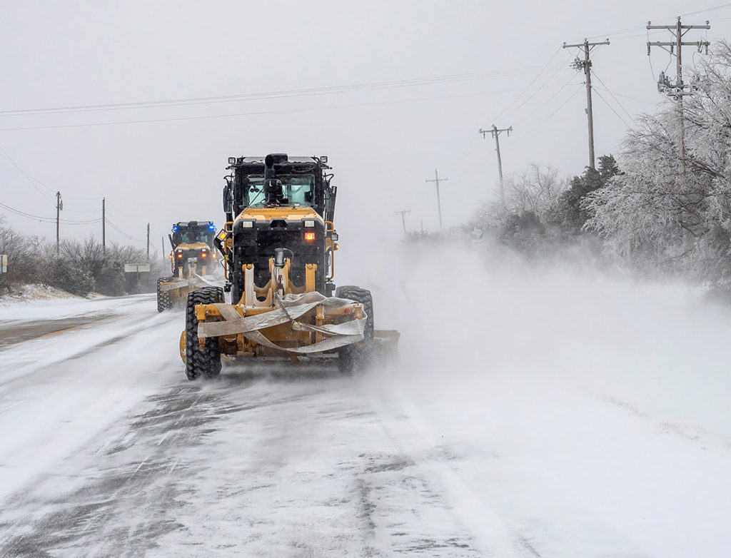 Two road graders remove snow and ice from road during winter storm.