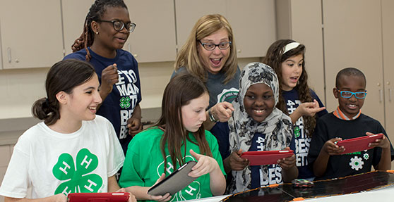 A group of students and teachers, several with green 4-H emblems on their shirts, work on ipads.
