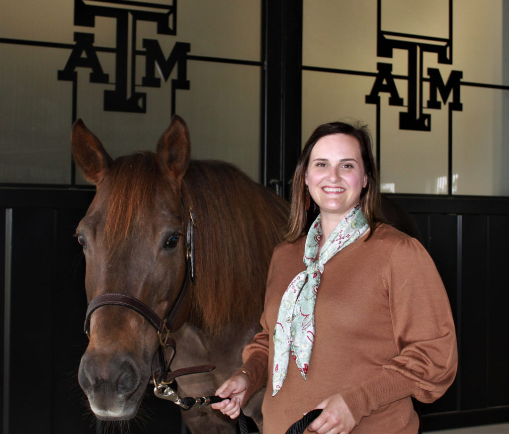 Jessica Leatherwood stands holding a horse with the Texas A&M logo in the background on windows in a barn area