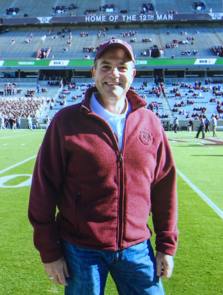 Gary Wingenbach wearing a Texas A&M hat and jacket standing on football field