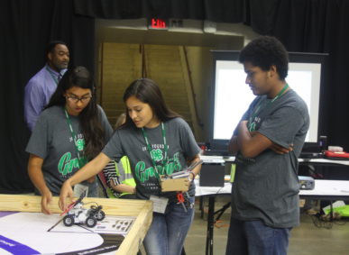 Group of 4-H teens with a small robot with wheels on a table