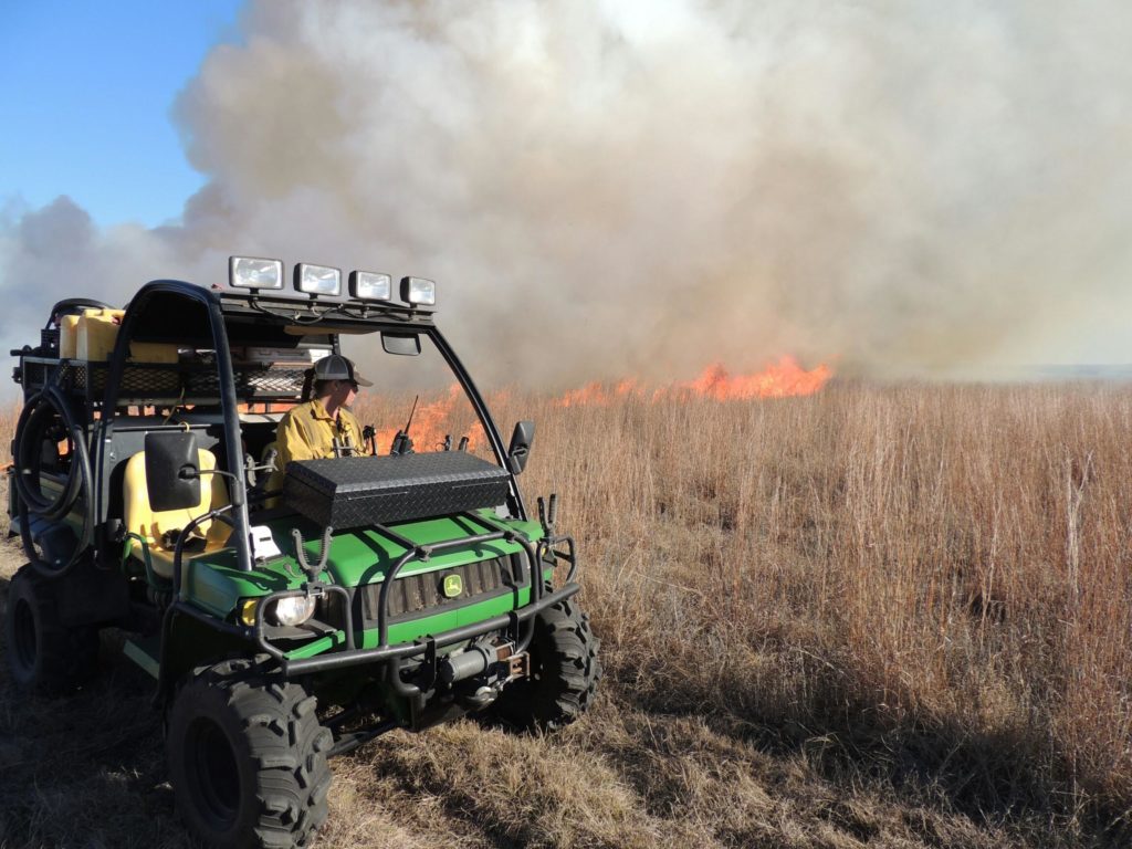 A prescribed burn fire behind a polaris vehicle with a person behind the wheel observing the burn