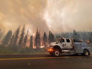 Fire engine in roadway with trees and fire in the background in western states wildfires