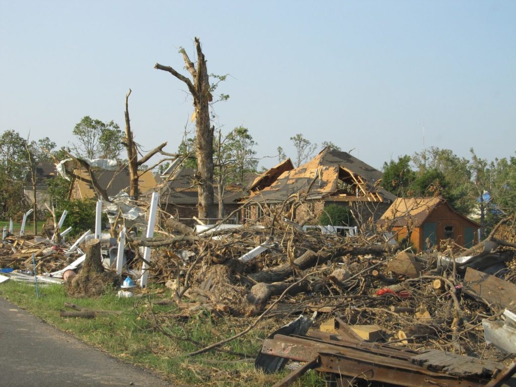 Damage from hurricane depicted by broken and toppled trees and homes missing parts of their roof.