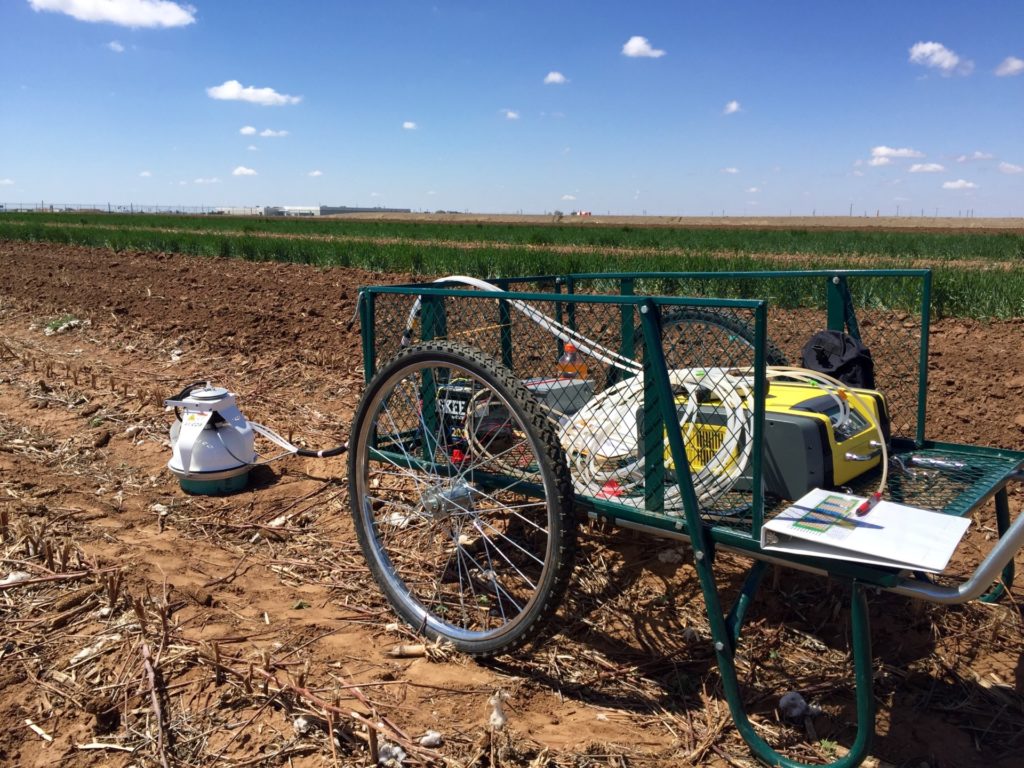 A small white piece of equipment sits in a field - it will measure greenhouse gas. A cart on bicycle tires hauls the equipment