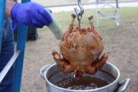 A blue-gloved hand inserts a thermometer to check the interior temperature of a deep-fried holiday turkey sitting over a pot of hot oil