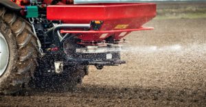 A red spreader on the back of a tractor shoots out fertilizer
