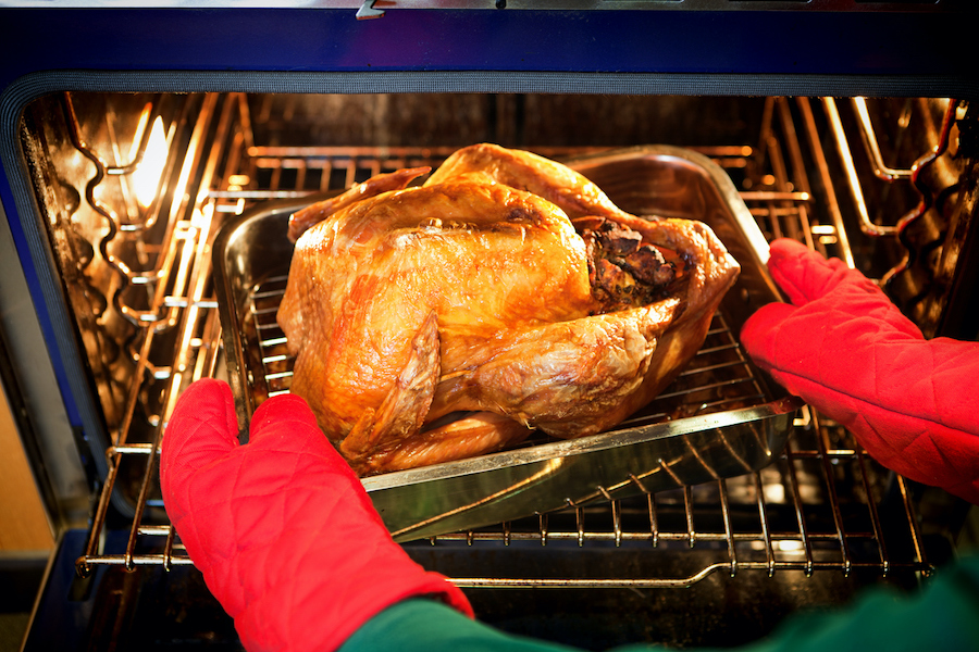 Brown roasted turkey being removed from oven with red oven mitts