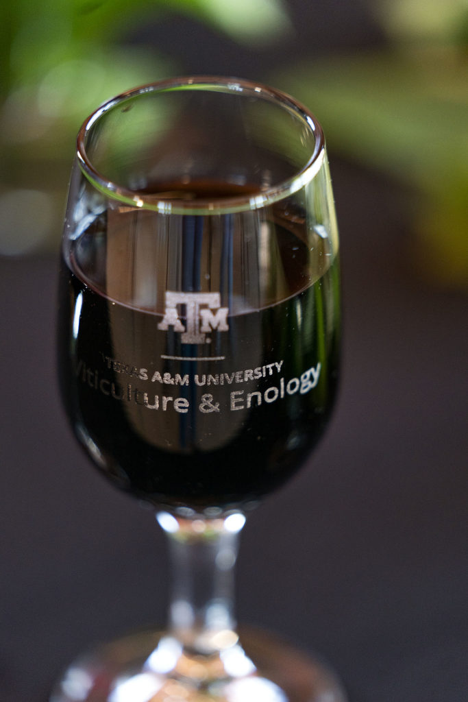A dark red wine in a glass with the Texas A&M University Viticulture and Enology written on it