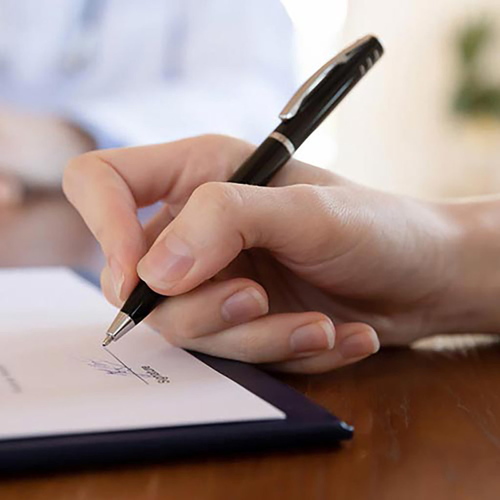 A hand holding a black pen preparing to sign a document as a part of estate planning.