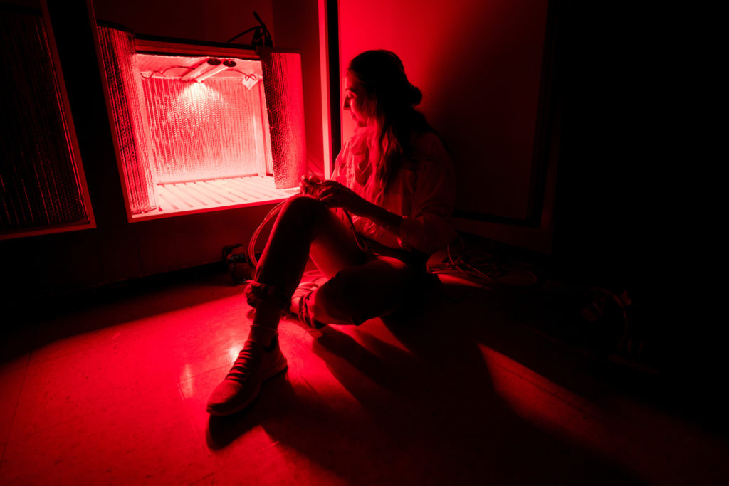 A woman sits in a red glow coming out of a light box