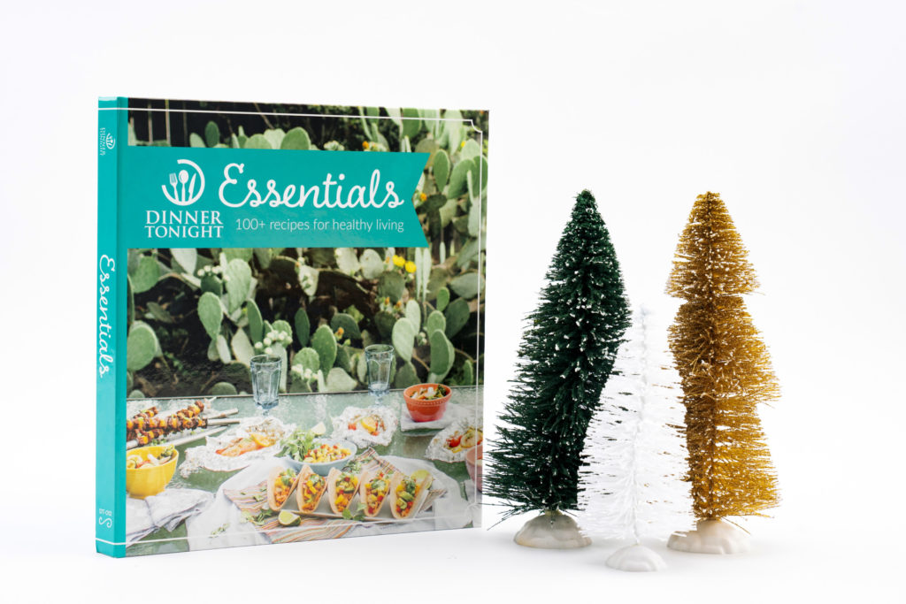 The Dinner Tonight Essentials cookbook is standing upright next to two fake Christmas trees