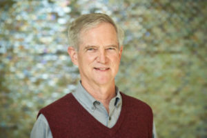 A smiling man in a sweater vest, John Mullet's professional photo