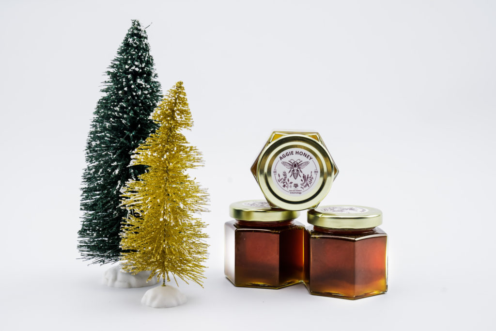 Two clear jars of Texas wildflower honey sit next two two small Christmas trees